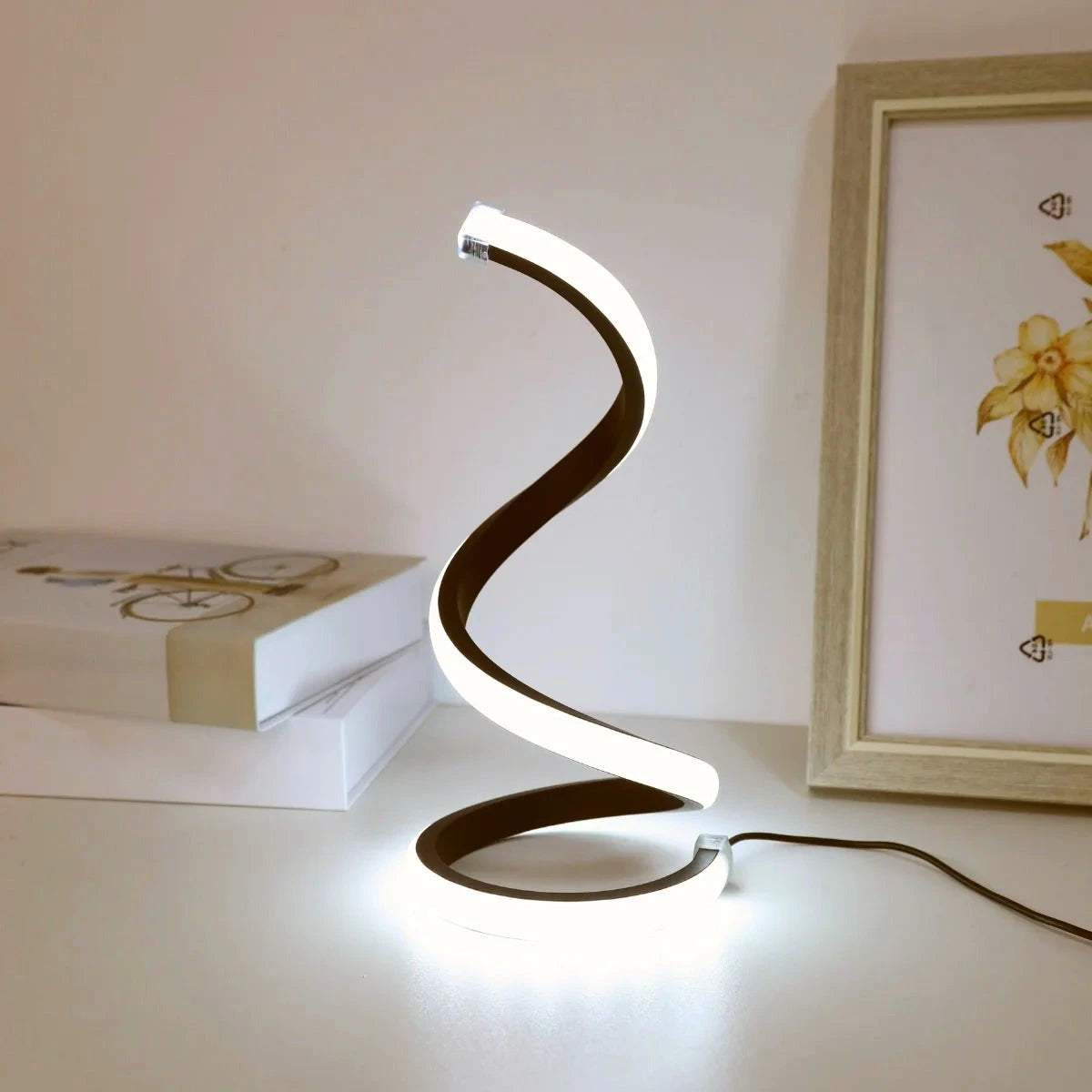Spiral LED table lamp in cool white mode on a desk beside a picture frame